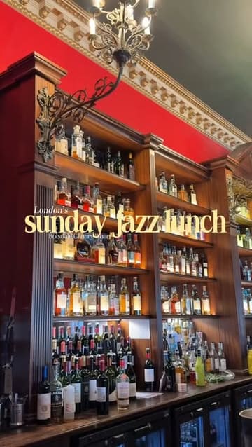 A high-quality, atmospheric shot of a well-stocked bar at Boisdale in Canary Wharf, featuring warm lighting and a classic, upscale aesthetic. The image effectively sets the scene for a Sunday jazz lunch, highlighting the venue's sophisticated interior.