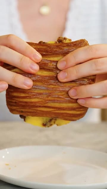 A close-up, first-person perspective shot of a laminated pastry being held by a person, promoting a new brunch menu at a venue in St John's Wood.