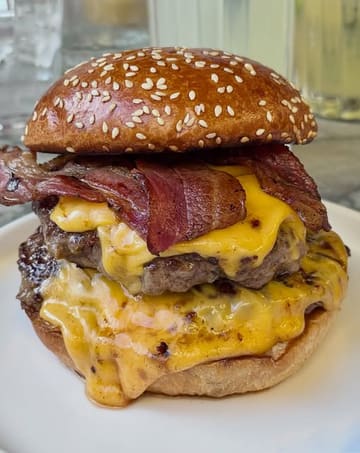 A high-quality, close-up shot of a double bacon cheeseburger, highlighting the melted cheese, crispy bacon, and toasted bun. The image is well-lit and focuses on the appetizing textures of the food.