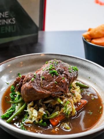 A close-up, appetizing shot of a slow-cooked beef shoulder dish served with vegetables and a rich gravy, presented in a rustic bowl.