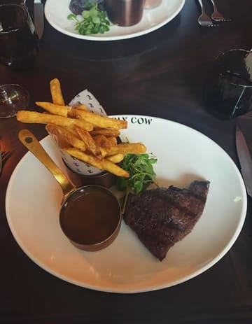 A standard, top-down restaurant shot of a steak dinner featuring a rump steak, fries, and peppercorn sauce. The image captures the meal in a casual dining setting, though the composition is slightly tight and lacks professional polish.