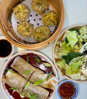 A high-quality, overhead food photography shot showcasing a variety of Chinese dishes, including steamed dumplings, beef cheung fun, and stir-fried greens. The lighting is bright and even, highlighting the textures and colors of the food, making for an appealing and professional-looking social media post.