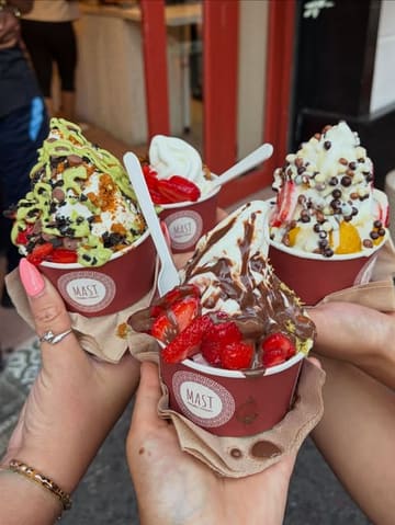 A bright, inviting shot of three cups of frozen yogurt held together in a 'cheers' formation, showcasing the variety of toppings available at the venue.
