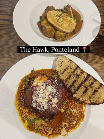 A top-down, overhead shot of two main courses served at The Hawk in Ponteland, featuring a pastry-topped dish and a square portion of lasagne with a side of grilled bread.
