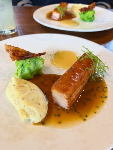 A high-quality, close-up shot of a slow-cooked pork belly dish served with grain mustard mash, hispi cabbage, and a cider sauce, captured at a restaurant.