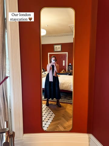 A mirror selfie taken in a boutique hotel room, showcasing the interior design and the creator's stay. The image captures the aesthetic of the room, including the red walls and wooden flooring.