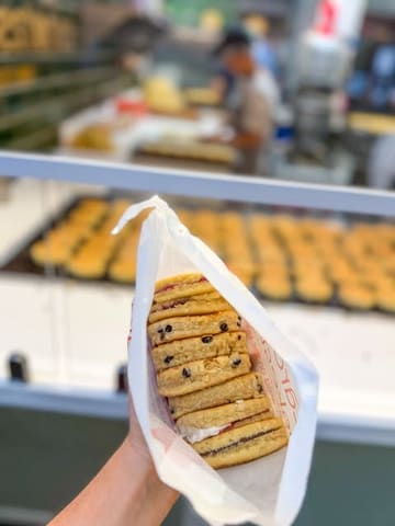 A close-up, handheld shot of a paper bag filled with Welsh cakes, captured at a market stall. The focus is sharp on the texture and filling of the cakes, effectively showcasing the product.