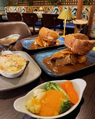 A high-angle shot of a Sunday roast spread at a restaurant, featuring plates of meat with large Yorkshire puddings, a side of cauliflower cheese, a side of vegetables, and an espresso martini in the background.