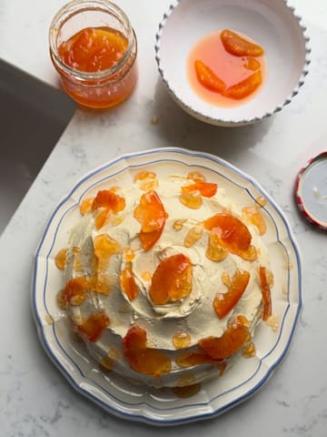 A top-down, high-quality shot of a homemade dome-shaped cake decorated with orange segments and marmalade, set on a marble surface.