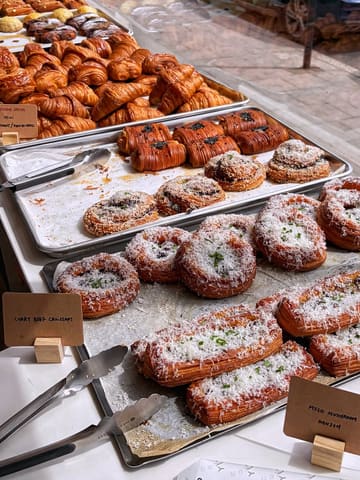 A clear, well-lit, and appetizing photograph of a bakery display case filled with a variety of freshly baked savoury and sweet pastries, including curry beef croissants and danishes, with clear labels for the items.