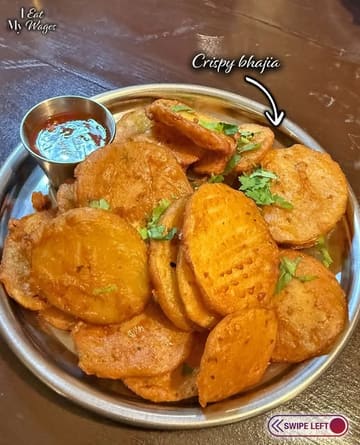 An overhead, close-up shot of a plate of crispy bhajia served with a side of dipping sauce, presented on a simple metal plate on a wooden table.