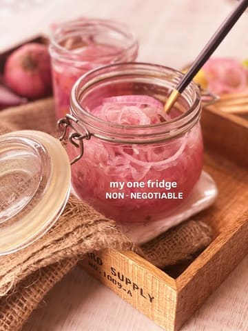 A high-quality, aesthetically pleasing food photography shot of pickled red onions in a glass jar, presented on a rustic wooden tray with burlap. The image is well-lit and styled to look like a professional food blog or recipe post.