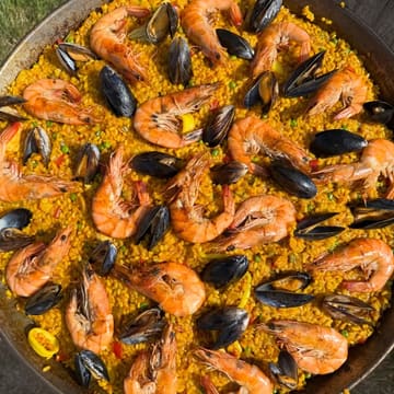 A vibrant, overhead shot of a homemade seafood paella served in a traditional pan, featuring well-cooked rice, large prawns, and mussels.