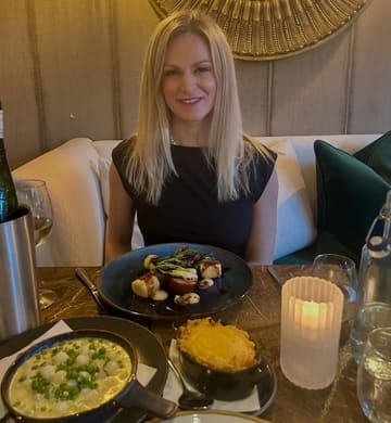 A photo of a diner at a restaurant table featuring a spread of dishes including suckling pig, potato gratin, and a pea-based side dish. The image captures a dining experience, likely for a review or social media post.