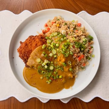 A clean, overhead shot of a homemade chicken katsu curry served with fried rice, garnished with spring onions. The image is bright and well-composed, focusing on the texture of the breaded chicken and the curry sauce.