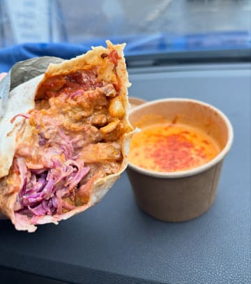 A casual, handheld shot of a burrito and a side of queso dip taken inside a car, showcasing the meal's contents.
