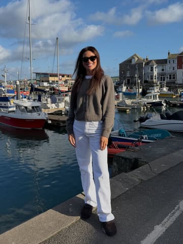 A bright, well-composed portrait of a woman standing on a harbour wall in Cornwall, used to promote a staycation experience.