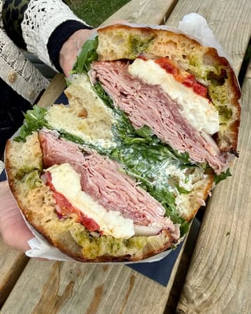 A high-quality, close-up shot of a generously filled focaccia sandwich held by a person, clearly displaying the fresh layers of cured meats, mozzarella, and greens.