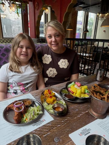 A candid, family-focused photograph taken at an Indian restaurant, showing a woman and a child at a table filled with various dishes, providing a relatable and authentic look at the dining experience.