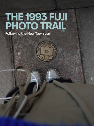 A first-person perspective shot looking down at a brass 'Fuji Photo Trail' plaque embedded in a grey pavement. The image is moody and atmospheric, capturing a local Edinburgh activity.