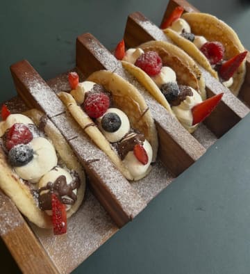 A high-quality, overhead shot of Nutella-filled taco pancakes served in a wooden rack, garnished with fresh strawberries, raspberries, and blueberries, dusted with icing sugar.