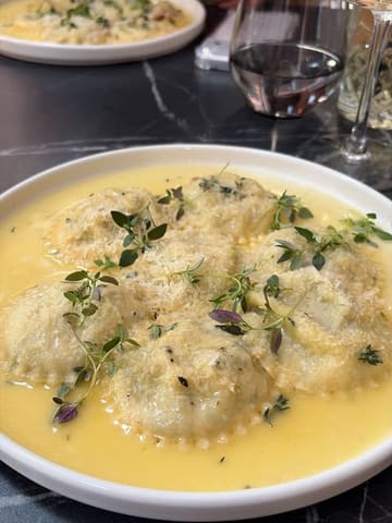 An overhead, close-up shot of a plate of ravioli served in a creamy sauce, garnished with fresh herbs, captured at an Italian restaurant.