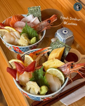 A bright, high-quality overhead shot of two Japanese donburi bowls featuring fresh sashimi, served with miso soup on a clean wooden table. The composition is balanced and the food presentation is highly appetising.