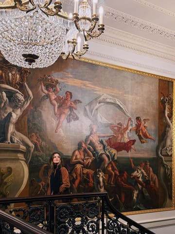 A high-quality, aesthetically pleasing portrait of a person standing on a grand staircase in front of a large, ornate Renaissance-style mural, evoking a sense of luxury and timelessness.