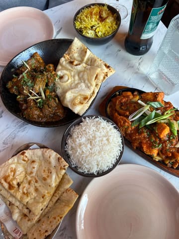A top-down, flat-lay photograph of an Indian meal spread featuring curries, rice, and naan bread, captured in a restaurant setting.