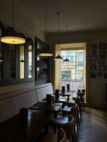 A clean, well-composed interior shot of a restaurant dining area. The image captures the warm, inviting atmosphere with wooden tables, comfortable seating, and soft lighting, creating a pleasant setting for a meal.