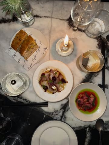 A high-quality, overhead flat-lay shot of a multi-course meal at a Japanese-Italian fusion restaurant, capturing an intimate, candlelit dining experience.