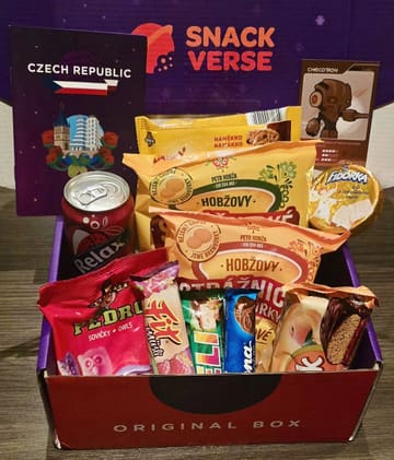 A straightforward, functional product shot of a 'Snackverse' subscription box featuring various Czech snacks, including crisps, gummies, and a drink. The image is taken from a high angle, showing the contents of the box against its branded packaging.