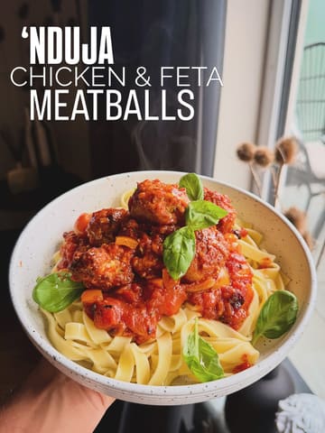 A high-quality, appetizing shot of a homemade pasta dish featuring 'nduja chicken and feta meatballs, presented in a bowl with fresh basil garnish. The image uses natural lighting and a shallow depth of field to highlight the texture of the sauce and meatballs.