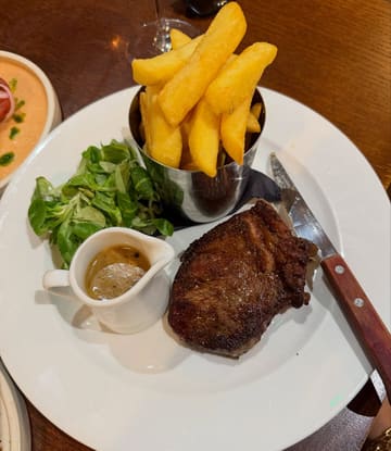 A straightforward, top-down photograph of a pub-style steak and chips meal served on a white plate with a side of salad and sauce.