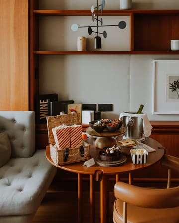 A high-quality, lifestyle-focused shot capturing an in-room hospitality experience at a luxury hotel. The image features a well-curated table setup including popcorn, snacks, a chocolate cake, and a wine bucket, suggesting a cozy, premium movie night or relaxation setting. The composition is balanced and inviting, highlighting the attention to detail in the hotel's service.
