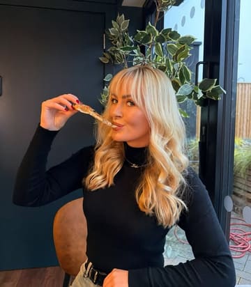 A casual, influencer-style shot of a woman eating a slice of pizza at a street food venue. The image captures a relaxed, social dining moment.