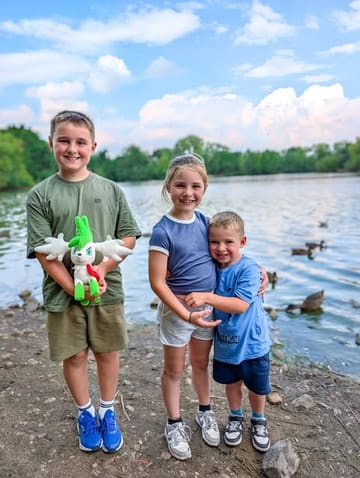 A bright, family-focused photograph taken at a park by a lake, capturing a day out with children.