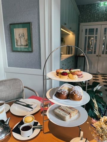 A high-quality, well-composed shot of an afternoon tea service at a hotel. The image captures the tiered stand clearly, with the food looking fresh and inviting, while the background provides a sense of place without distracting from the main subject.