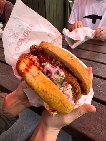 A close-up, eye-level shot of a chicken focaccia sandwich held in hands, showcasing the texture of the bread and the filling, set against an outdoor wooden table.