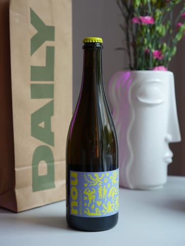 A clean, professional product shot featuring a bottle of 'nou secco brut' wine. The bottle is centered in the frame, flanked by a branded 'DAILY' paper bag and a decorative white vase with flowers, creating a lifestyle-focused aesthetic that feels intentional and well-styled.