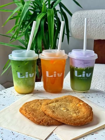 A bright, well-composed, and visually appealing shot of three colorful iced drinks and two cookies from Liv Cafe, effectively showcasing their summer menu offerings.