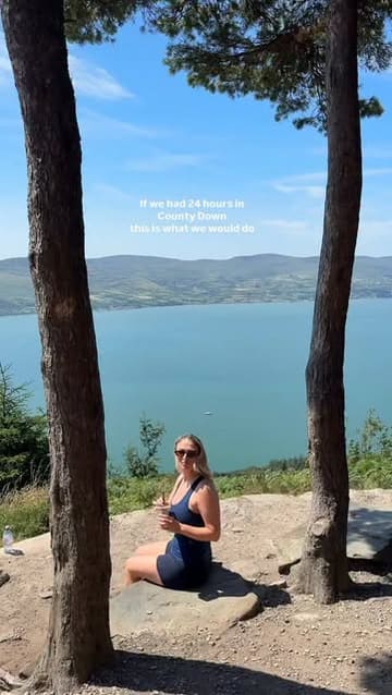 A travel-focused social media post featuring a scenic, outdoor lifestyle shot of a person enjoying a coffee with a view of a lough in County Down. The image serves as an introduction to a listicle itinerary for a 24-hour trip.