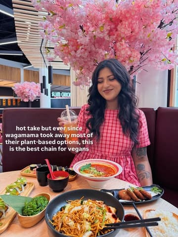 A social media post featuring a person dining at a restaurant with a spread of Japanese dishes, including ramen and sushi, with artificial cherry blossom decor in the background.