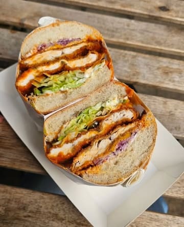 A close-up, high-angle shot of a chicken sandwich cut in half, served in a takeaway box on a wooden table.