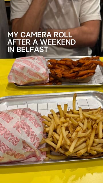 A casual, overhead-style photo of two trays of burgers and fries from Bunsen, captured during a weekend trip to Belfast. The image features the brand's signature bright yellow table and simple, no-frills presentation.