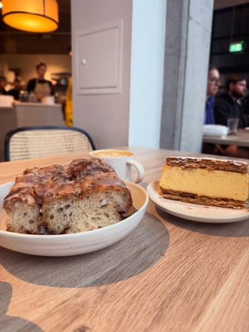 A high-quality, well-lit shot of a cafe table featuring a pastry and a mille-feuille, accompanied by a coffee. The composition is clean and inviting, capturing the atmosphere of a relaxed cafe visit with a shallow depth of field that keeps the focus on the food.