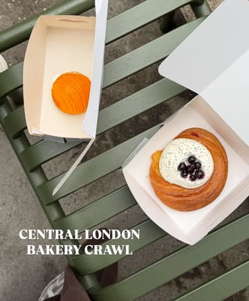 A clean, overhead shot of two pastries in takeaway boxes resting on a green metal bench, captured during a Central London bakery crawl. The lighting is bright and natural, highlighting the textures of the pastries.