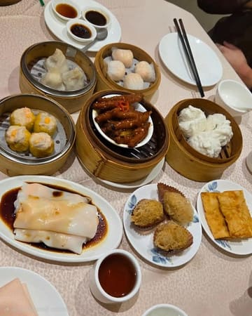 A top-down, overhead shot of a dim sum spread on a restaurant table, featuring various bamboo steamers and plates containing dumplings, buns, and chicken feet.