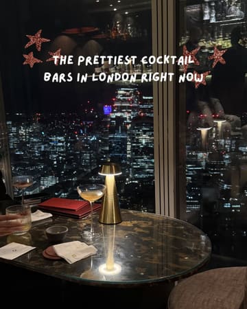 A moody, atmospheric shot of a cocktail bar table at night, featuring a view of the London skyline. The image uses a table lamp to illuminate the drinks and menu, creating a romantic and upscale vibe suitable for a listicle about cocktail bars.