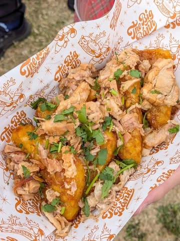 A close-up, top-down shot of pork belly loaded hash browns served in branded paper at a food festival, capturing the texture and freshness of the street food.